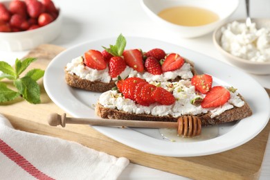 Photo of Delicious ricotta bruschettas with strawberry, mint, pistachios served with honey on white table