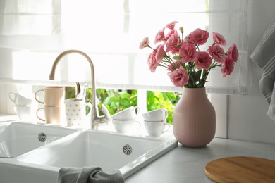 Photo of Vase with flowers on countertop near sink against window in kitchen