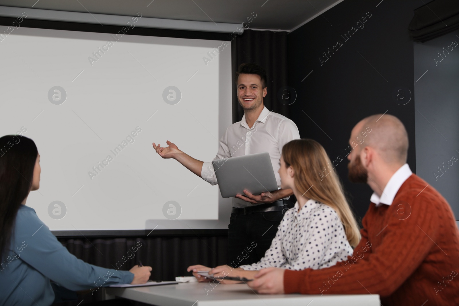 Photo of Business people listening to speaker in conference room with video projection screen