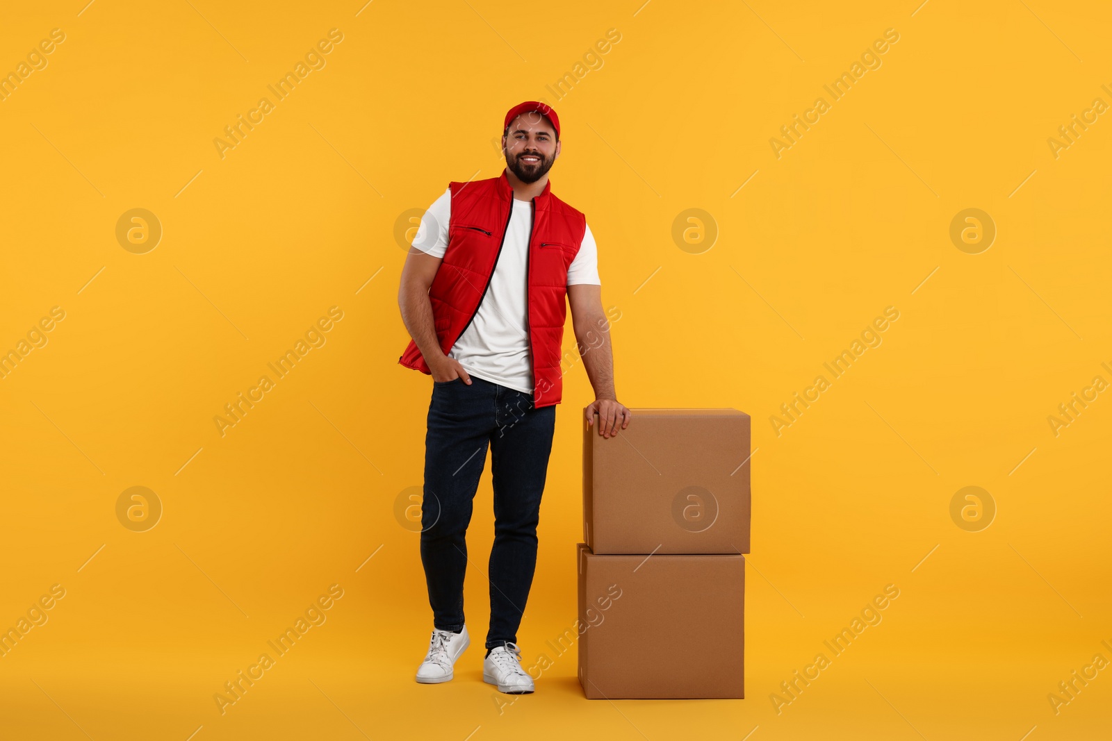 Photo of Happy young courier with parcels on orange background