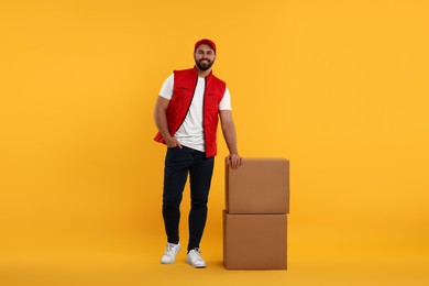 Happy young courier with parcels on orange background