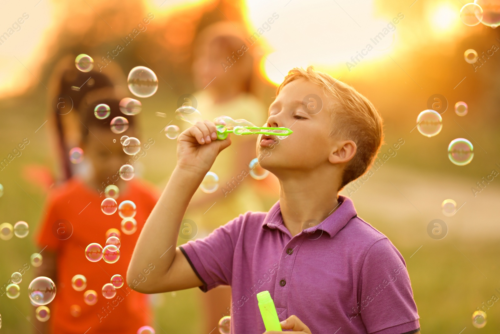 Image of Cute little boy blowing soap bubbles outdoors at sunset