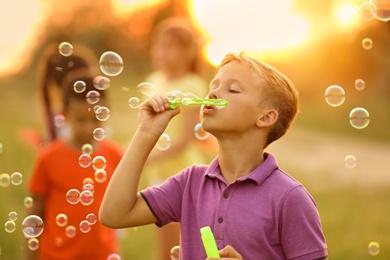 Image of Cute little boy blowing soap bubbles outdoors at sunset