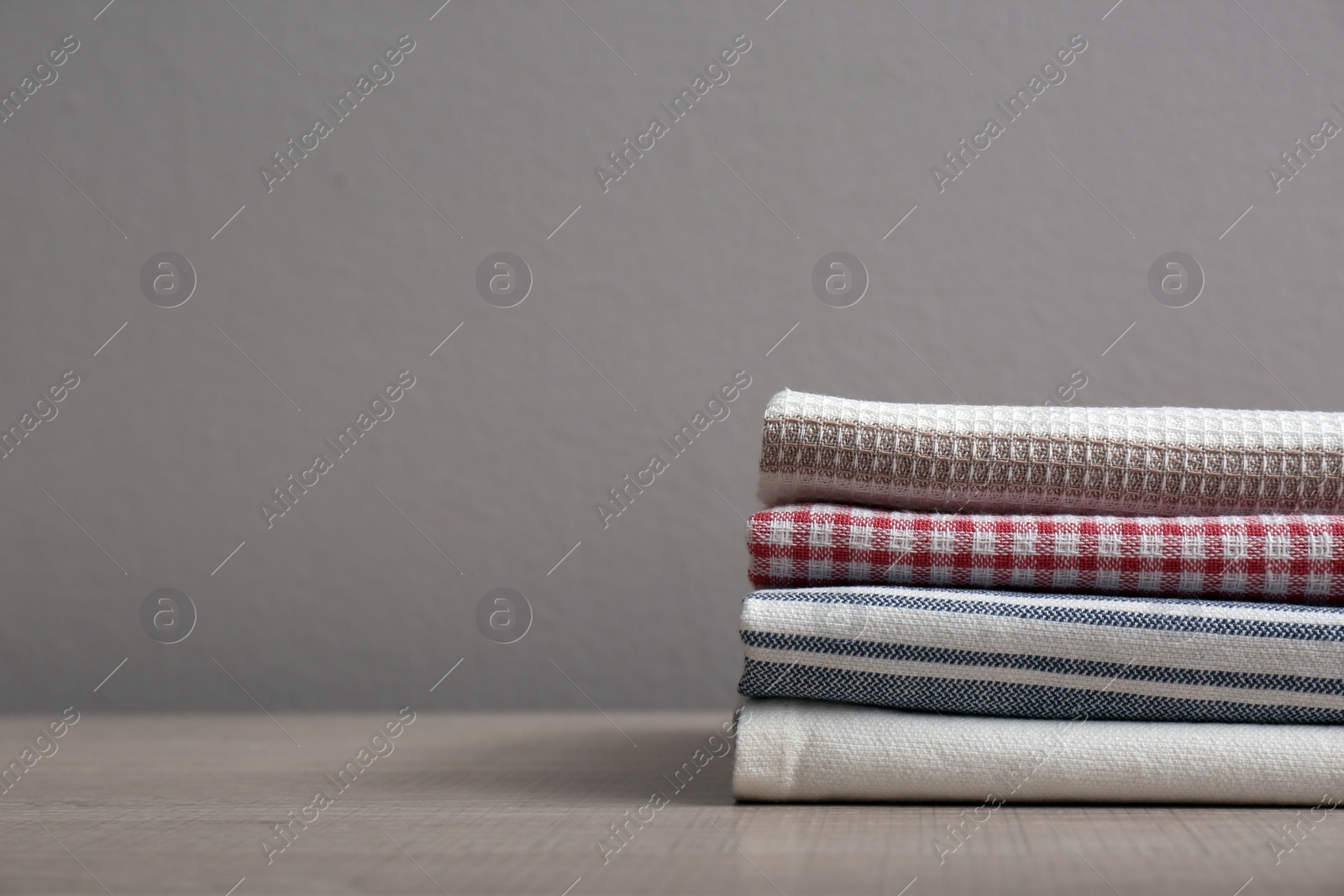 Photo of Stack of soft kitchen towels on wooden table against grey background, space for text