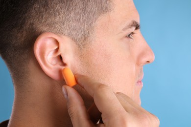 Photo of Man inserting foam ear plug on light blue background, closeup