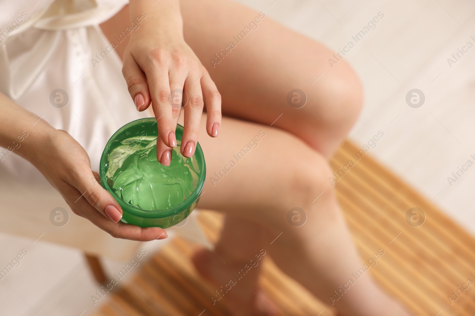 Photo of Young woman holding jar of aloe gel indoors, closeup. Space for text