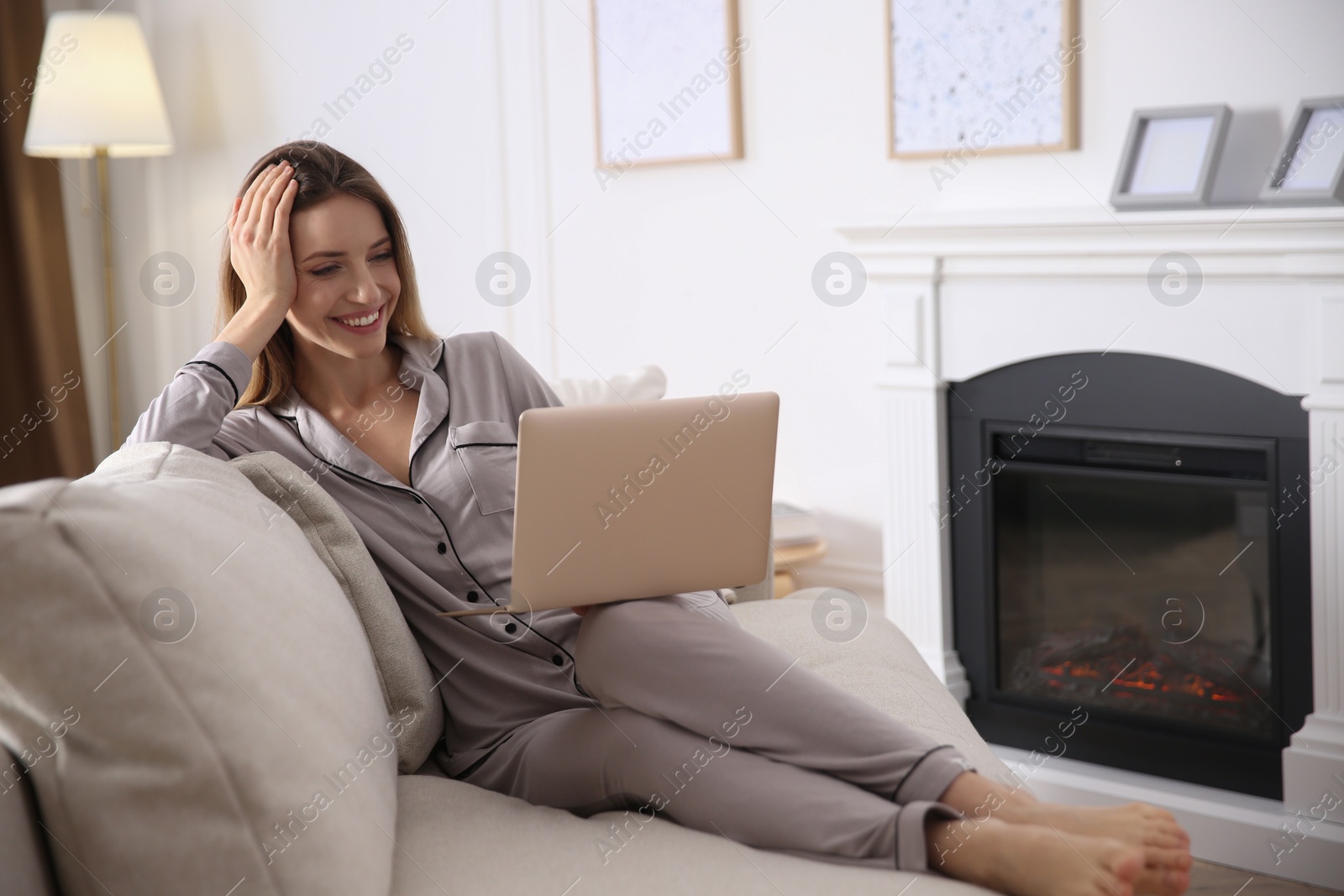 Photo of Young woman with laptop on sofa near fireplace at home