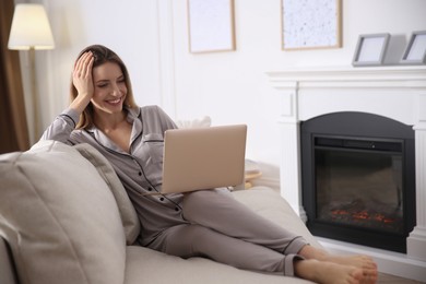 Young woman with laptop on sofa near fireplace at home