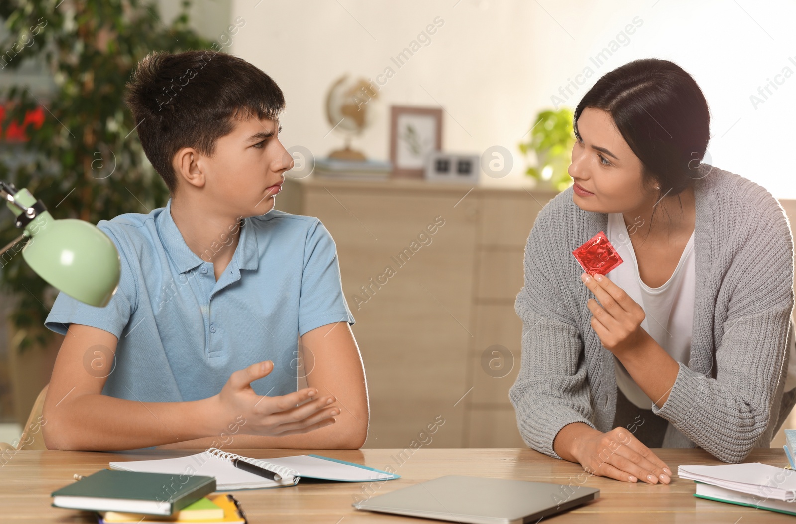 Photo of Mother talking with her teenage son about contraception while he doing homework at home. Sex education concept