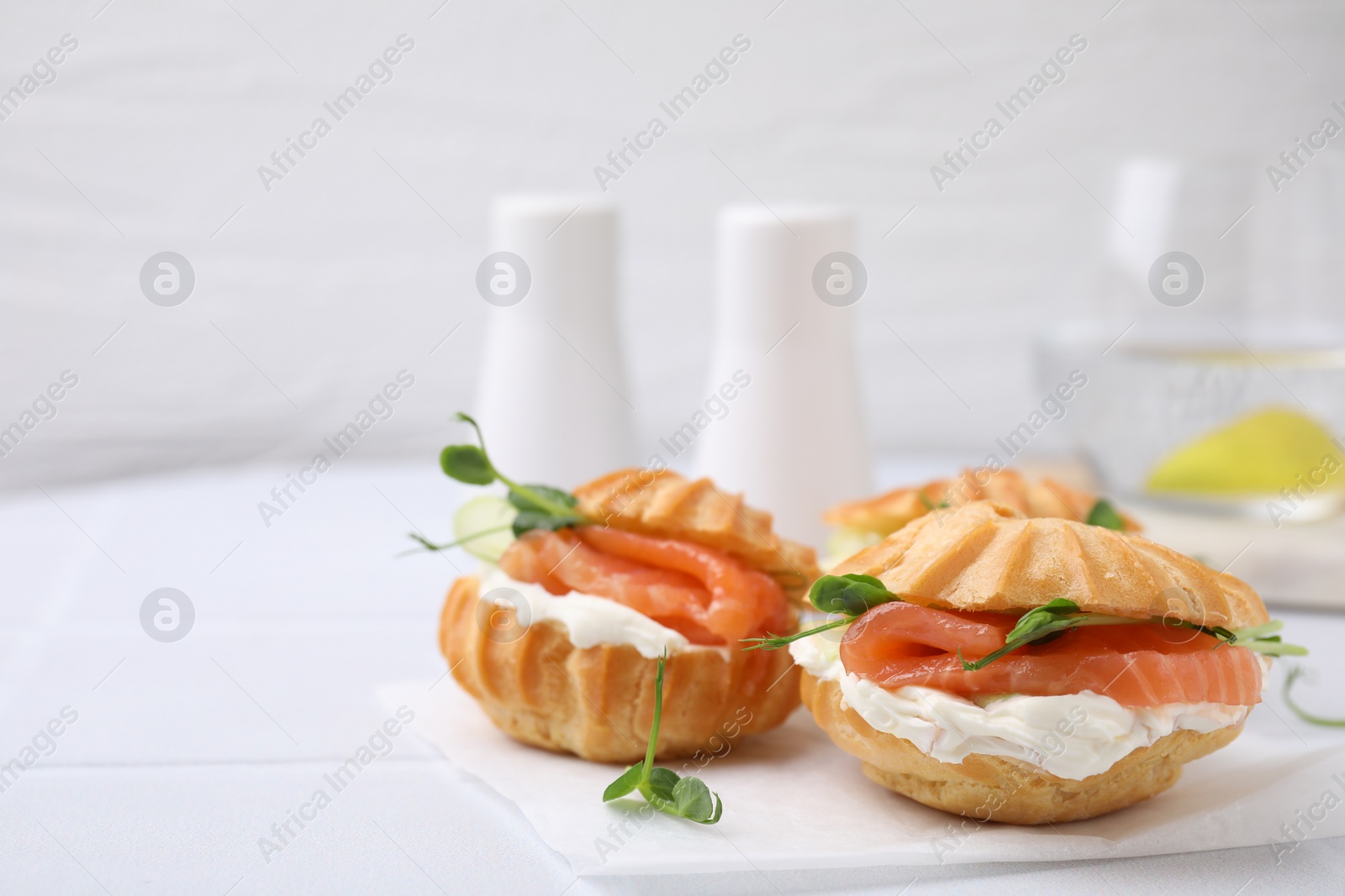 Photo of Delicious profiteroles with cream cheese and salmon on white table, closeup. Space for text