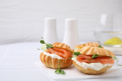 Photo of Delicious profiteroles with cream cheese and salmon on white table, closeup. Space for text