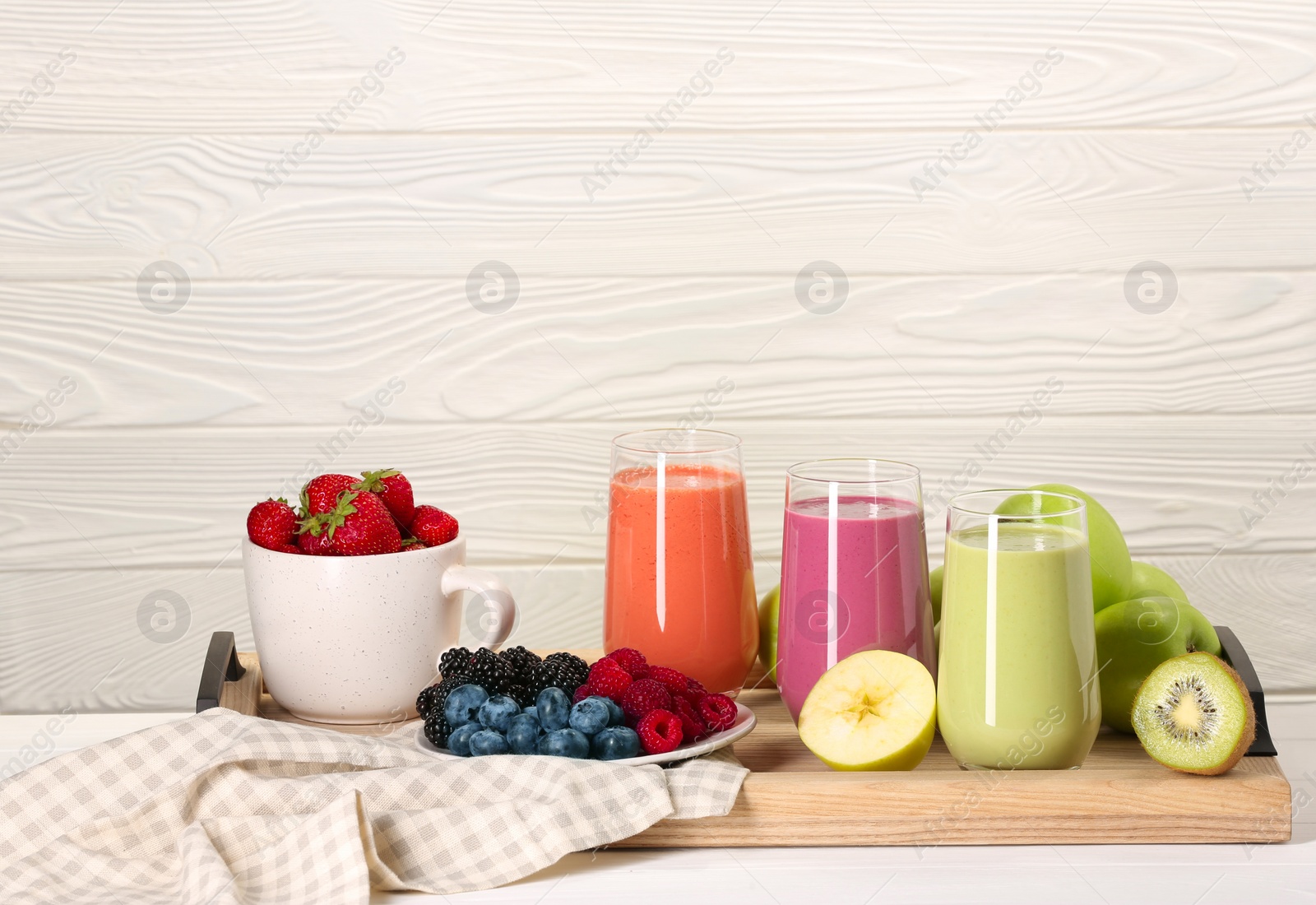 Photo of Glasses of different tasty smoothies and fresh ingredients on white wooden table