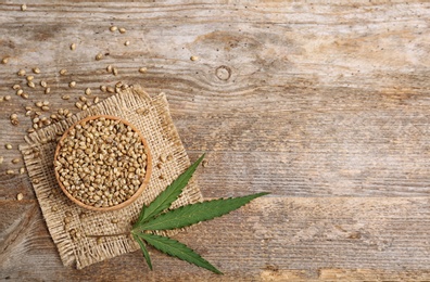 Photo of Bowl of hemp seeds and space for text on wooden background, top view