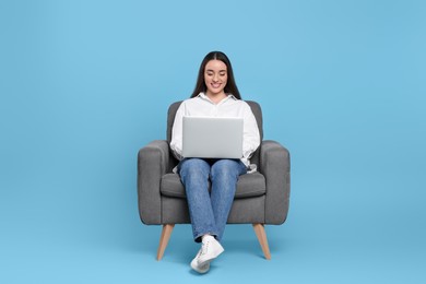 Photo of Smiling young woman working with laptop in armchair on light blue background