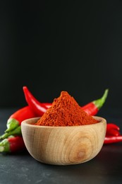 Photo of Paprika powder and fresh chili peppers on black table. Space for text