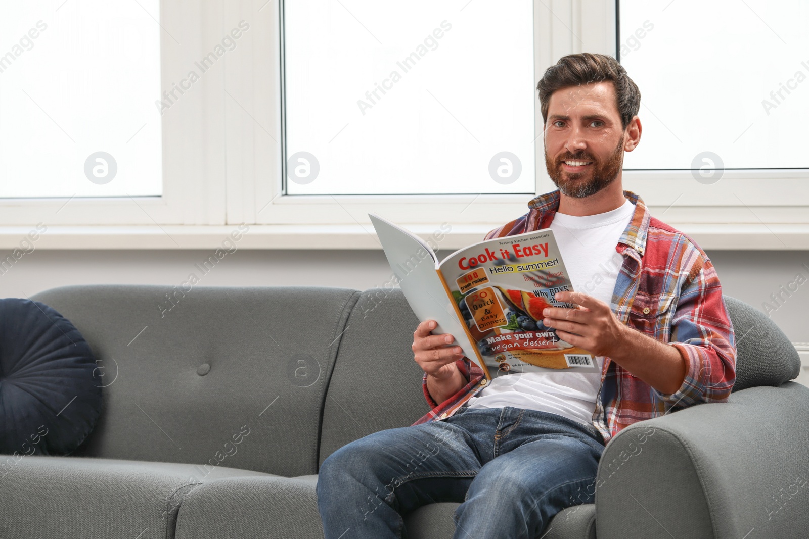 Photo of Smiling bearded man with magazine on sofa indoors