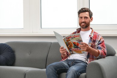 Smiling bearded man with magazine on sofa indoors