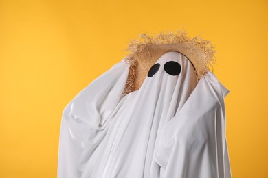 Person in ghost costume and straw hat on yellow background