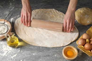 Woman rolling raw dough at grey table, closeup