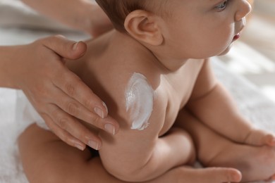 Photo of Mother applying body cream on her little baby at home, closeup