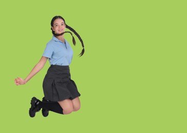 Image of Happy girl in school uniform jumping on light green background, space for text