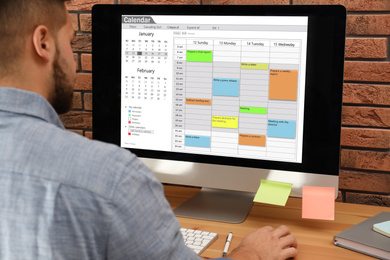 Young man using calendar app on computer in office, closeup