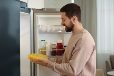 Man putting bowl covered with beeswax food wrap into refrigerator in kitchen
