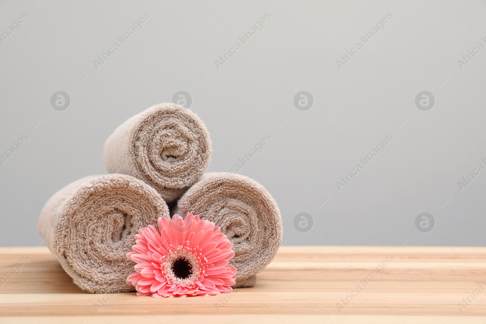 Photo of Stack of rolled towels and flower on table. Space for text