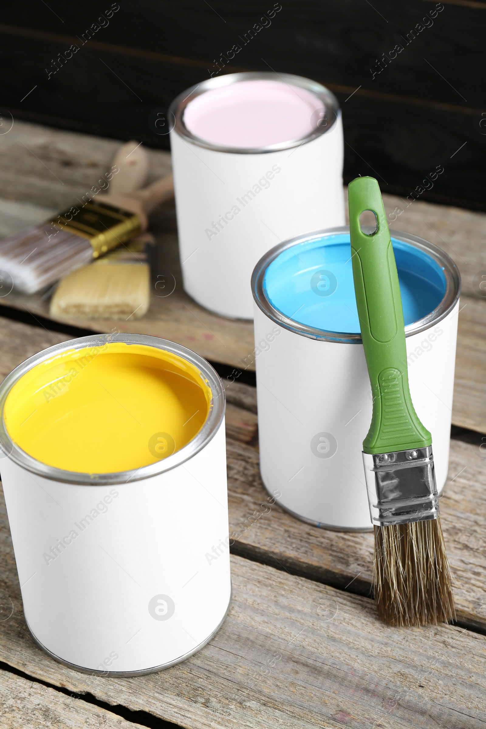 Photo of Cans of colorful paints with brushes on wooden table