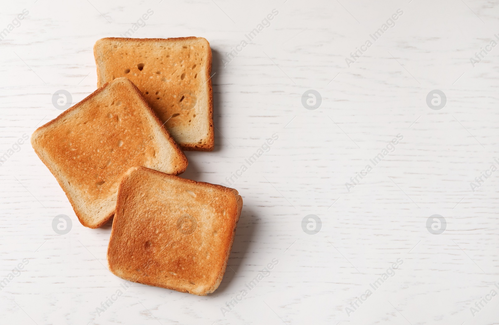 Photo of Slices of delicious toasted bread on white wooden table, top view. Space for text