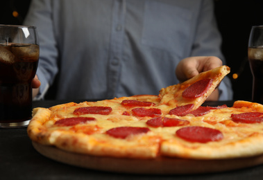 Photo of Woman taking tasty pepperoni pizza at table, closeup