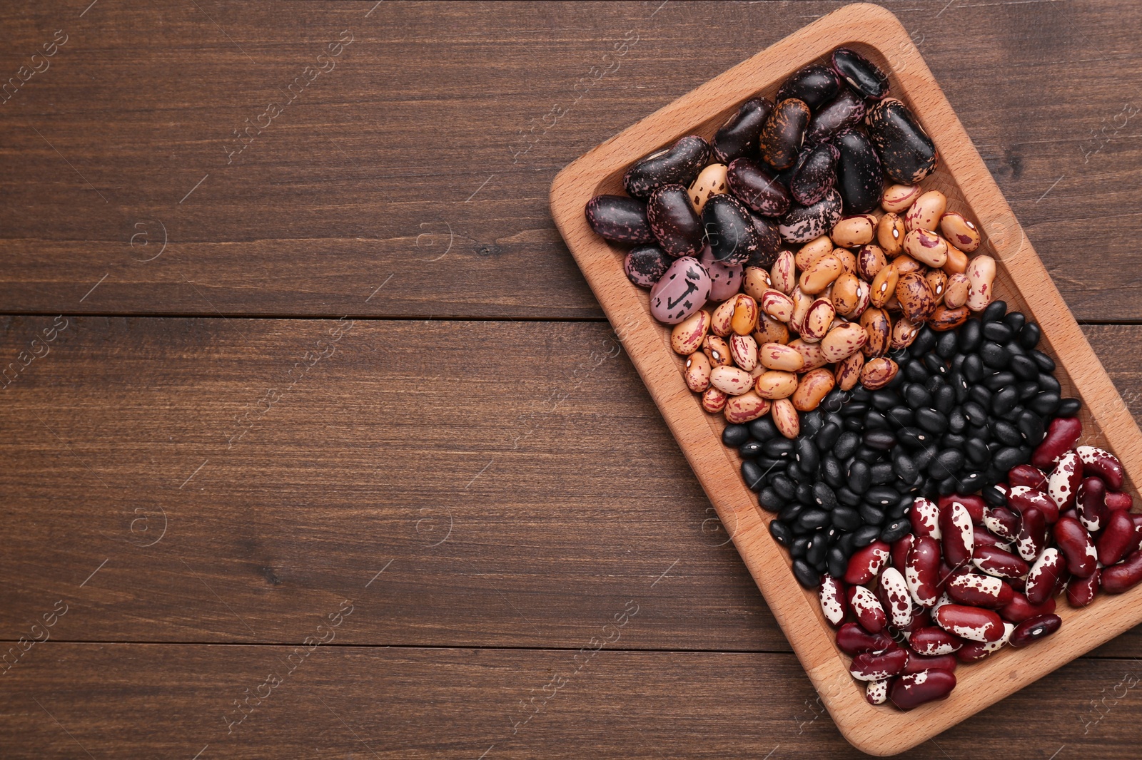 Photo of Plate with different kinds of dry kidney beans on wooden table, top view. Space for text