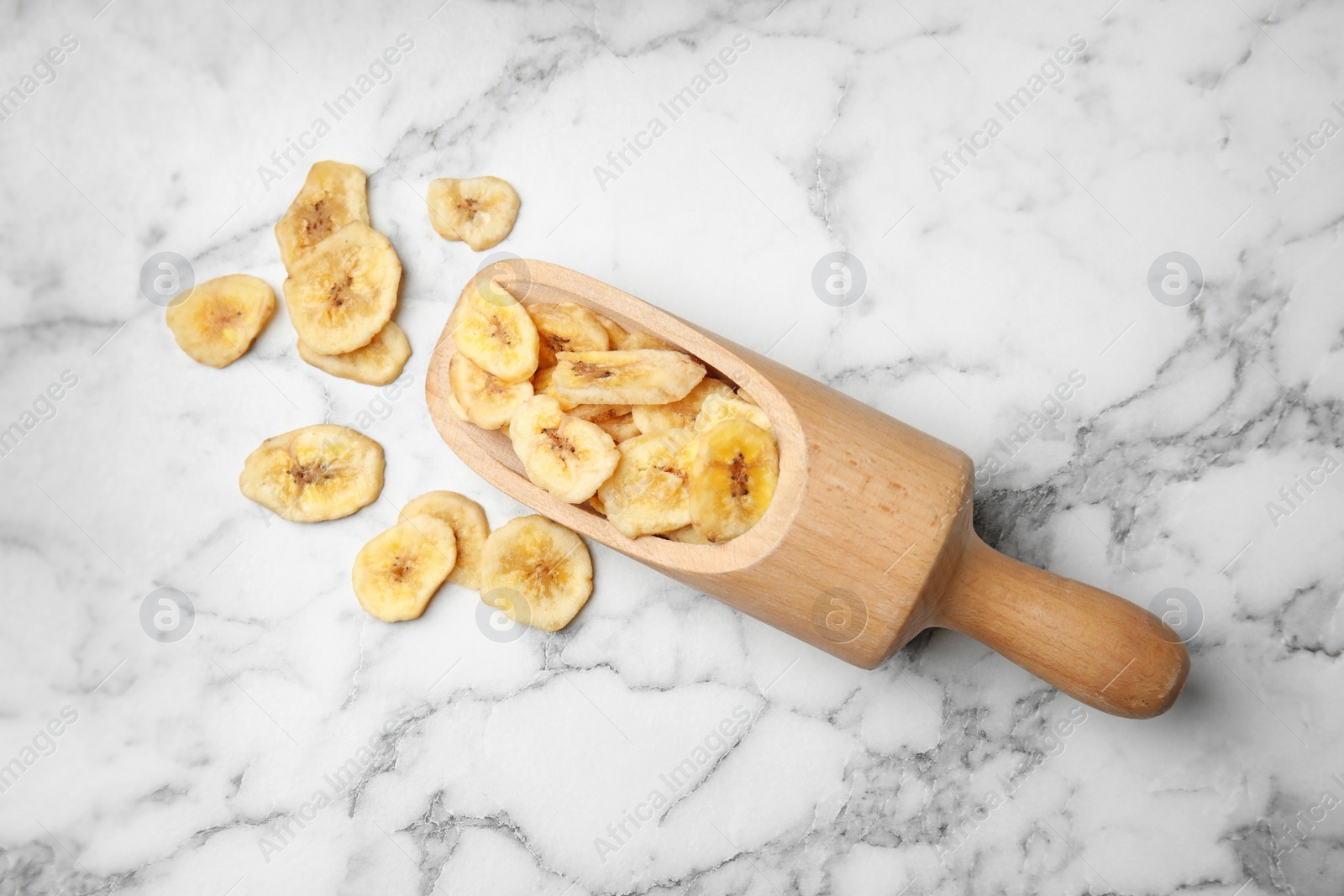 Photo of Scoop with banana slices on marble background, top view. Dried fruit as healthy snack