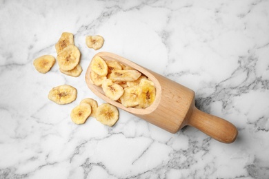 Photo of Scoop with banana slices on marble background, top view. Dried fruit as healthy snack