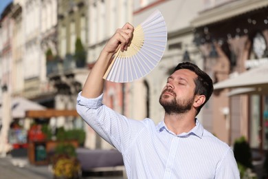 Man with hand fan suffering from heat outdoors