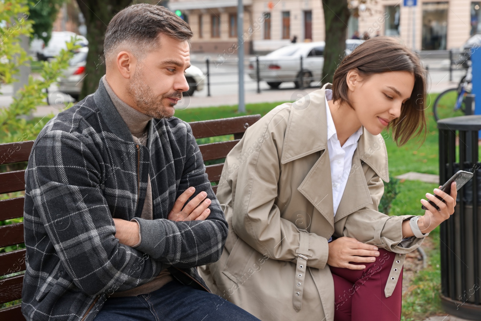 Photo of Distrustful man peering into girlfriend's smartphone outdoors. Relationship problems