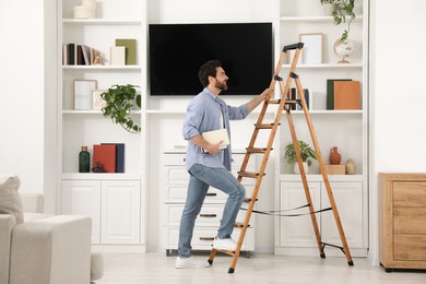 Photo of Man with books climbing on wooden folding ladder at home
