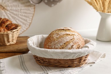 Wicker bread basket with freshly baked loaf on white marble table in kitchen