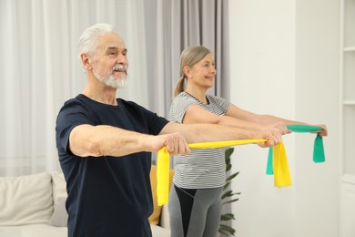 Photo of Senior couple doing exercise with fitness elastic bands at home, selective focus