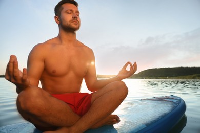 Man meditating on blue SUP board on river at sunset