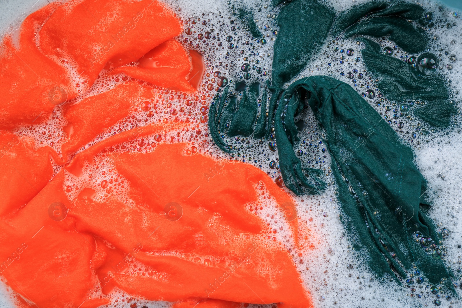 Photo of Colorful clothes in suds, top view. Hand washing laundry