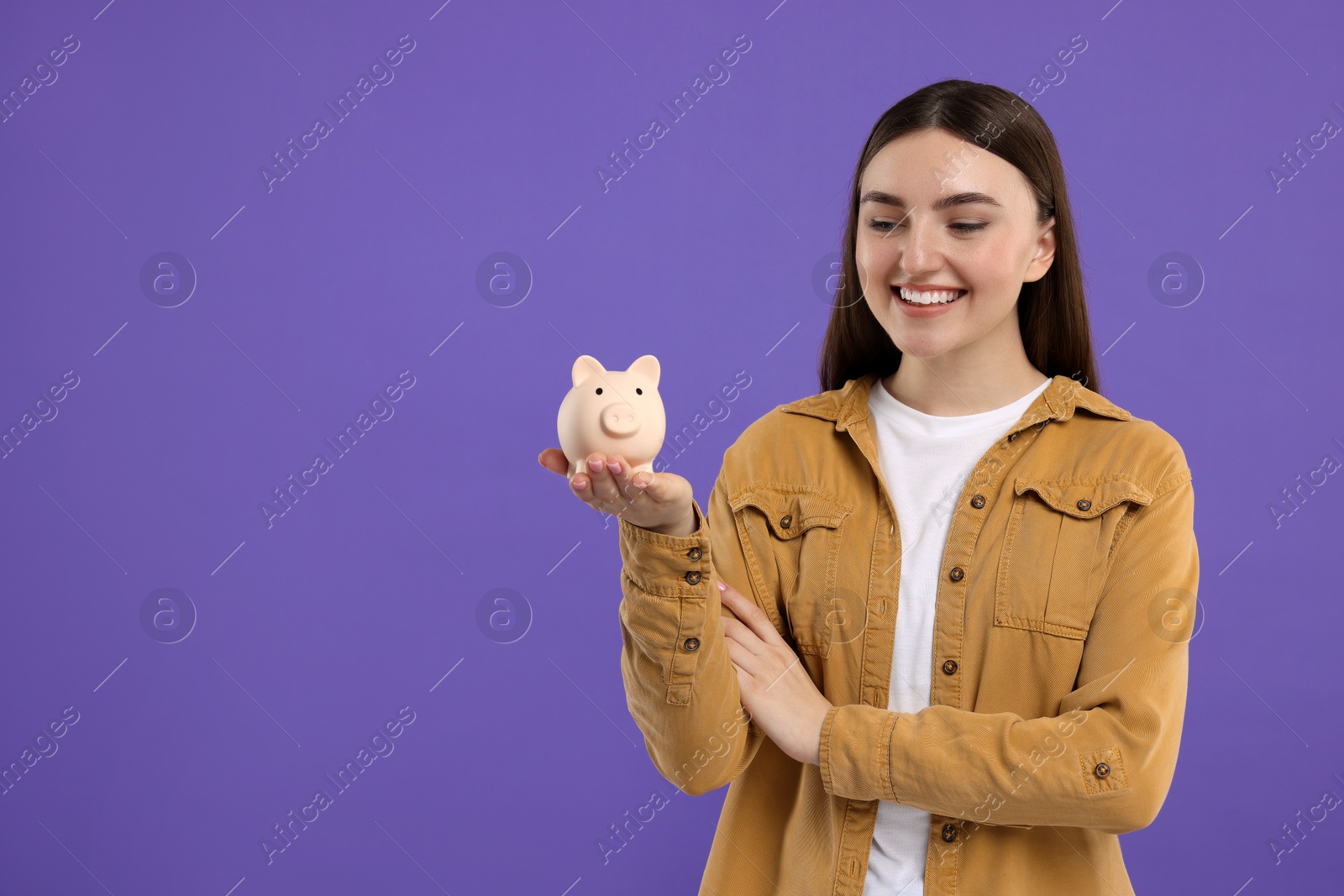 Photo of Happy woman with piggy bank on purple background, space for text