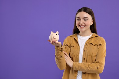 Photo of Happy woman with piggy bank on purple background, space for text