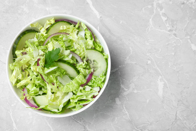 Photo of Tasty salad with cabbage and cucumbers on light grey marble table, top view. Space for text