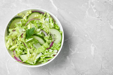 Tasty salad with cabbage and cucumbers on light grey marble table, top view. Space for text