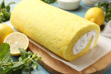 Photo of Delicious cake roll, mint and lemons on table, closeup