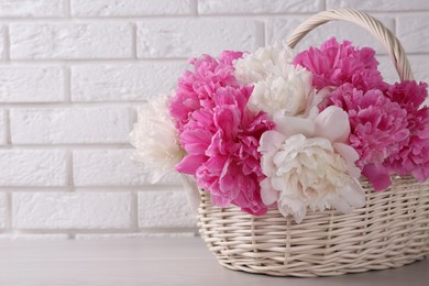Beautiful peonies in wicker basket on table near white brick wall. Space for text
