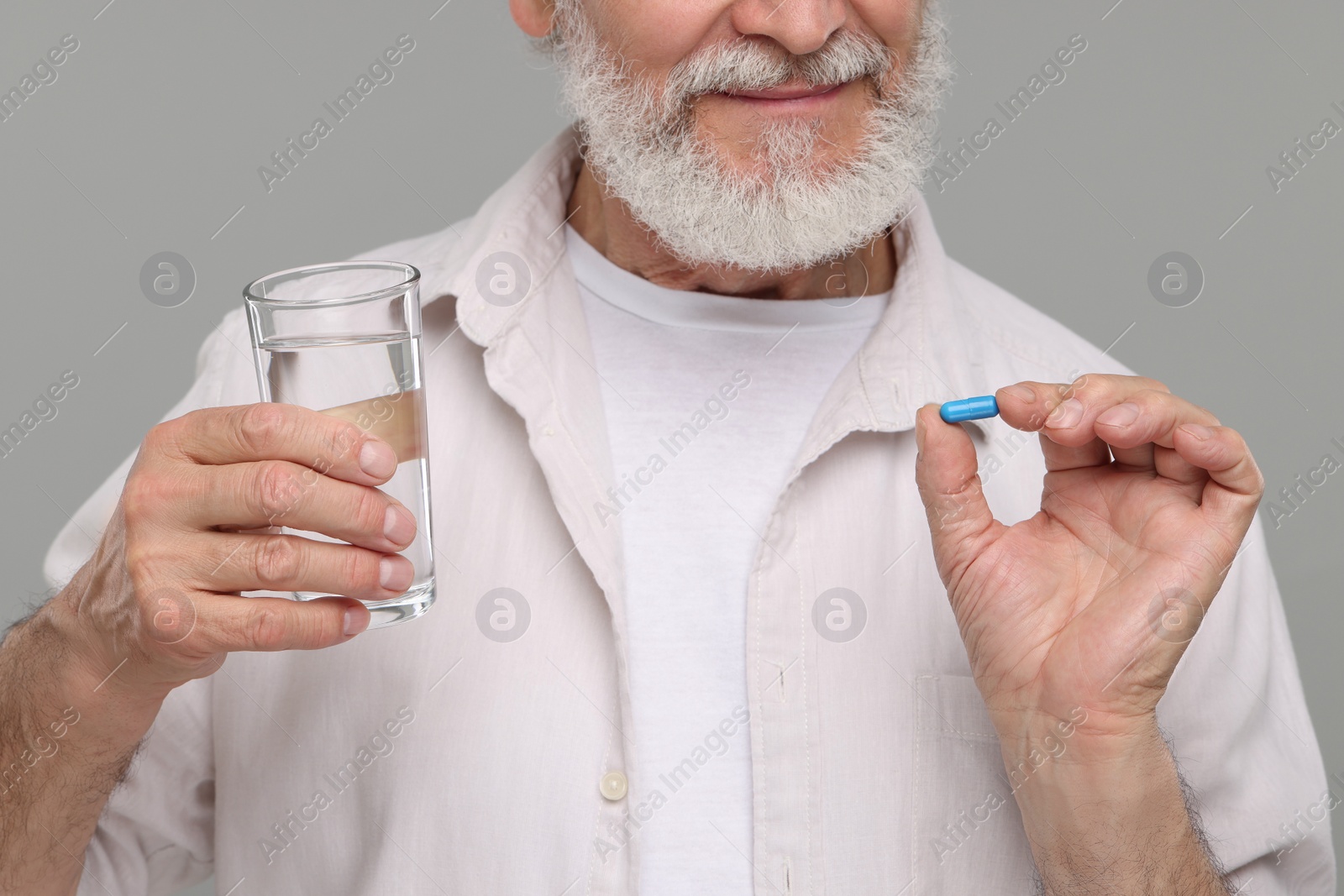Photo of Senior man with glass of water and pill on grey background, closeup