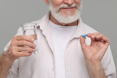 Photo of Senior man with glass of water and pill on grey background, closeup