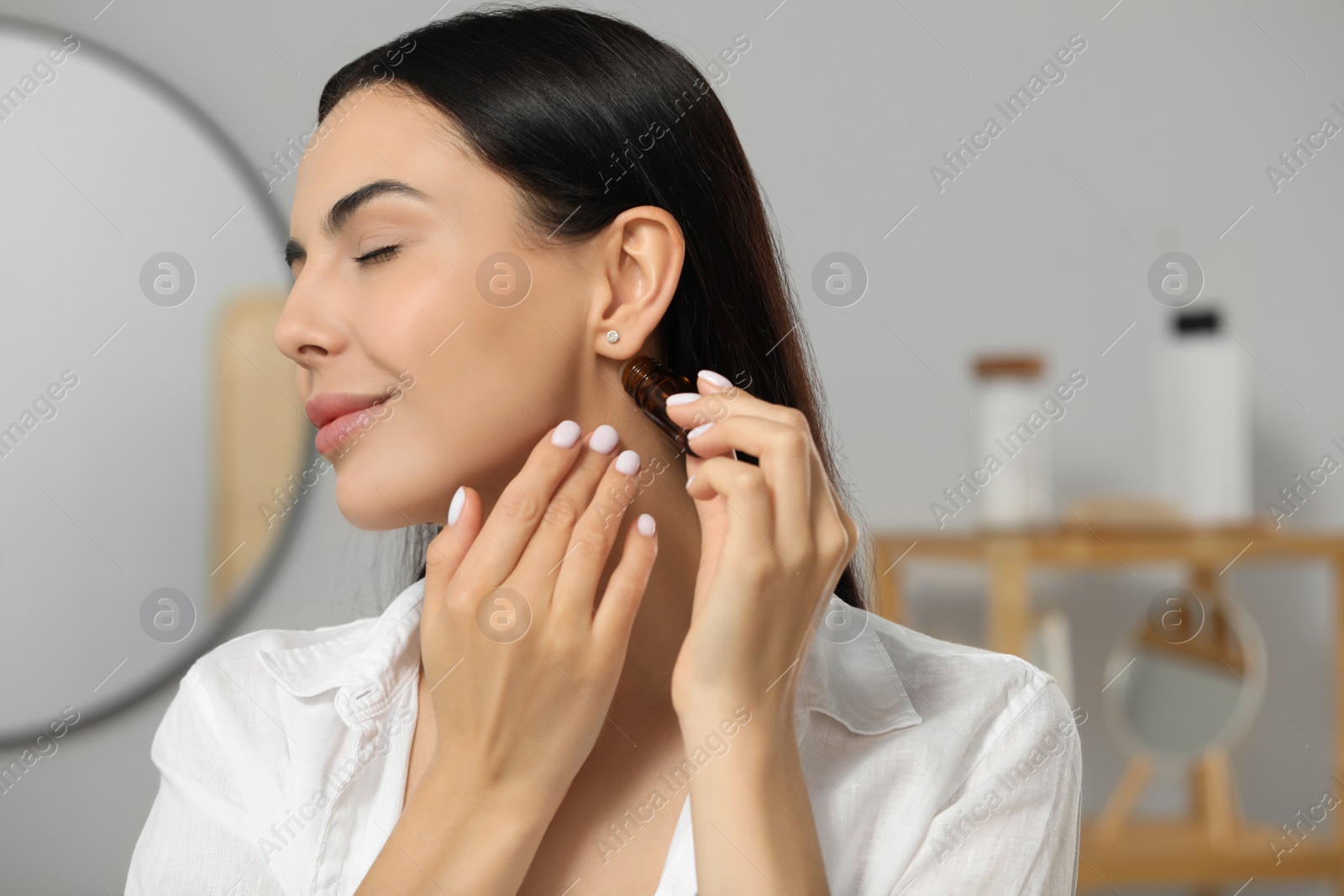 Photo of Young woman applying essential oil on neck indoors